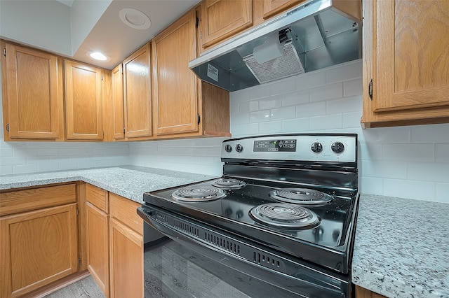 kitchen with light stone countertops, black range with electric cooktop, tasteful backsplash, and range hood