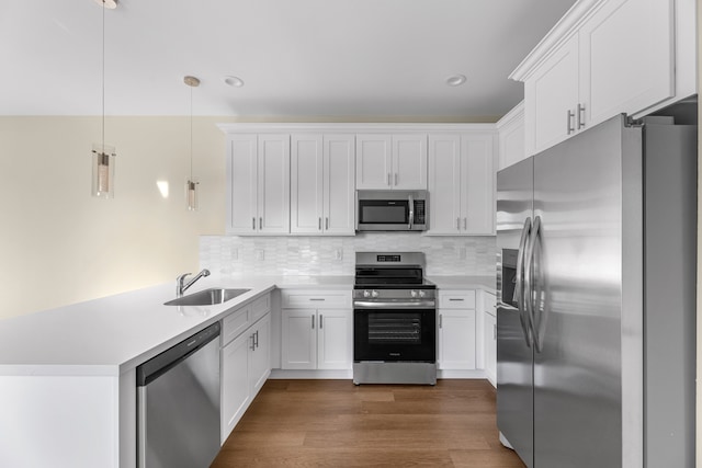 kitchen with white cabinetry, sink, hanging light fixtures, stainless steel appliances, and dark hardwood / wood-style floors