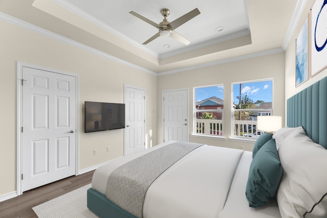 bedroom with ornamental molding, a tray ceiling, ceiling fan, and dark wood-type flooring