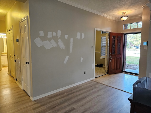 entryway with a textured ceiling, light hardwood / wood-style flooring, and ornamental molding