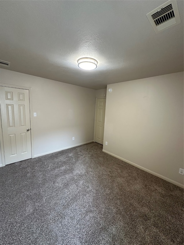 unfurnished room featuring a textured ceiling and dark colored carpet