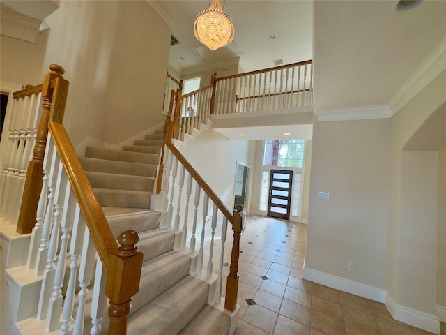 staircase with tile patterned floors, a towering ceiling, an inviting chandelier, and crown molding