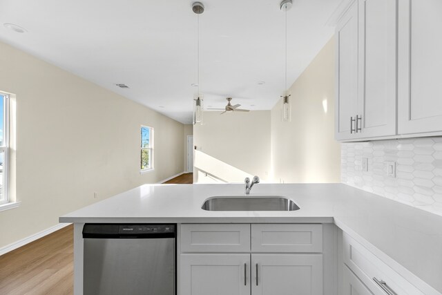 kitchen with sink, stainless steel dishwasher, kitchen peninsula, light hardwood / wood-style floors, and decorative light fixtures