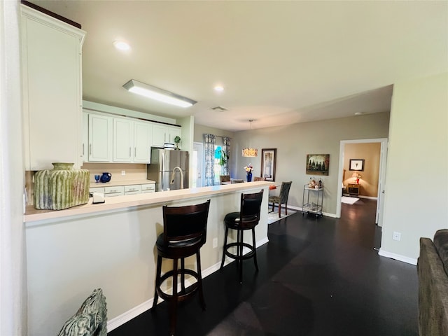 kitchen featuring a breakfast bar, an inviting chandelier, kitchen peninsula, stainless steel fridge, and white cabinetry