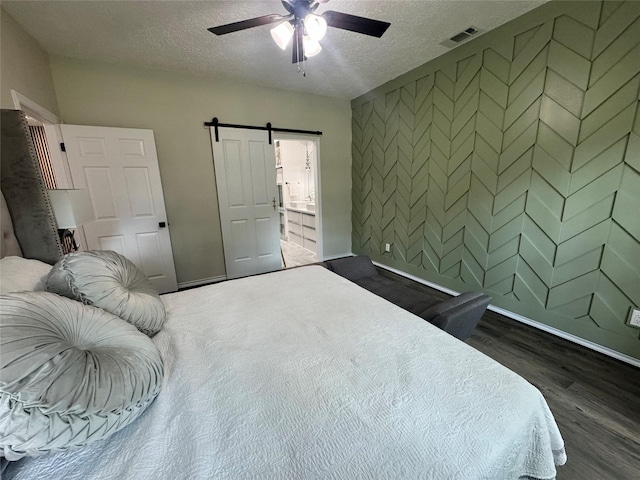 bedroom featuring ceiling fan, dark wood-type flooring, a barn door, and a textured ceiling