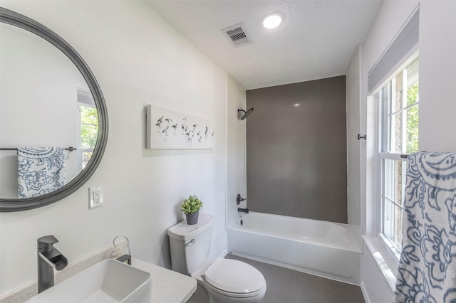 full bathroom with toilet, vanity, a textured ceiling, and tiled shower / bath combo