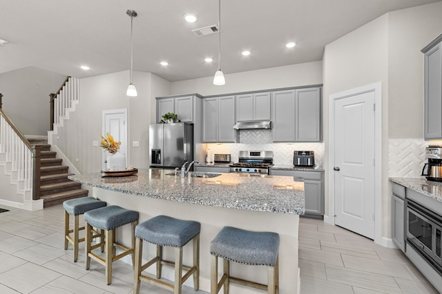 kitchen with gray cabinets, a kitchen island with sink, decorative light fixtures, and appliances with stainless steel finishes