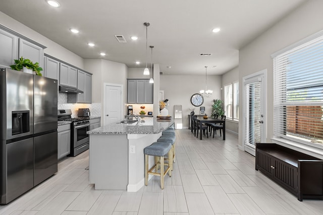 kitchen with a breakfast bar area, gray cabinetry, a center island with sink, and appliances with stainless steel finishes