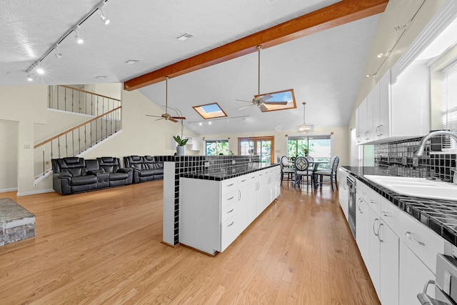 kitchen featuring white cabinets, light wood-type flooring, a skylight, and sink