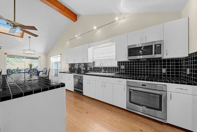 kitchen with tile countertops, decorative backsplash, vaulted ceiling with beams, white cabinetry, and stainless steel appliances