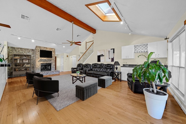 living room with beam ceiling, a skylight, rail lighting, and light hardwood / wood-style floors