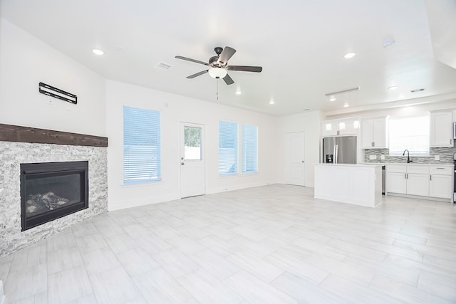 unfurnished living room with ceiling fan, a fireplace, and sink