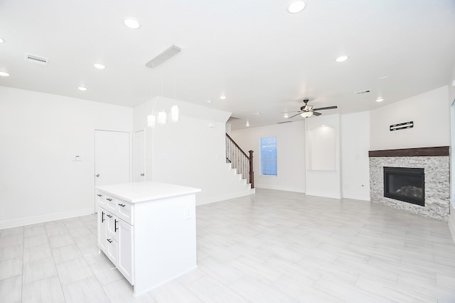 kitchen with hanging light fixtures, ceiling fan, a fireplace, a kitchen island, and white cabinetry