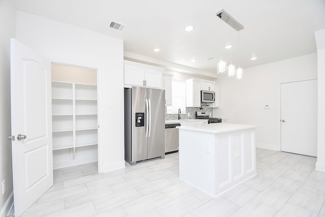 kitchen with appliances with stainless steel finishes, tasteful backsplash, a kitchen island, decorative light fixtures, and white cabinetry