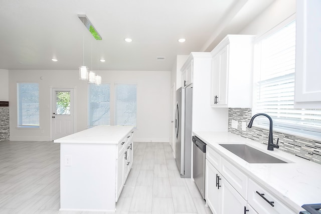 kitchen with light stone countertops, a center island, sink, stainless steel appliances, and white cabinets