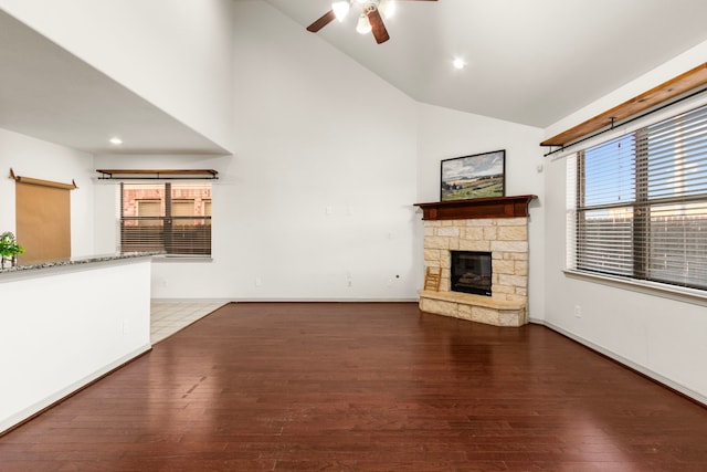 unfurnished living room with hardwood / wood-style flooring, ceiling fan, a stone fireplace, and high vaulted ceiling