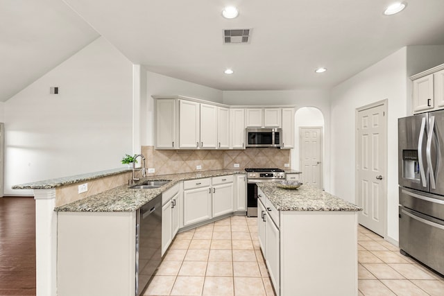 kitchen featuring kitchen peninsula, stainless steel appliances, a kitchen island, and light stone countertops