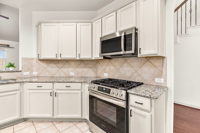 kitchen featuring stainless steel appliances, light stone counters, decorative backsplash, white cabinets, and light wood-type flooring