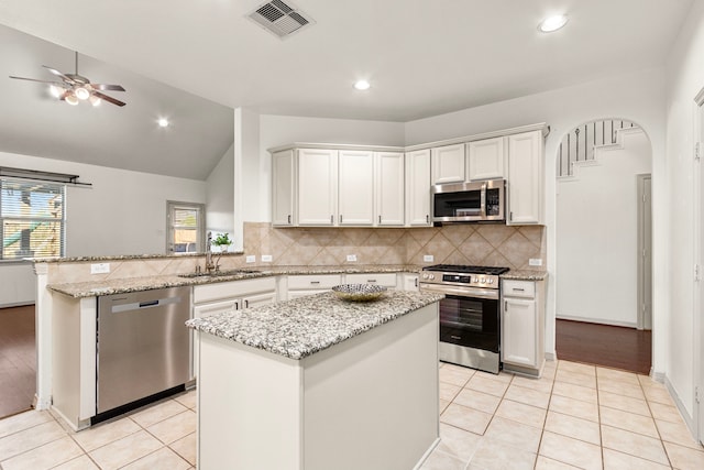 kitchen with kitchen peninsula, stainless steel appliances, vaulted ceiling, white cabinets, and a kitchen island