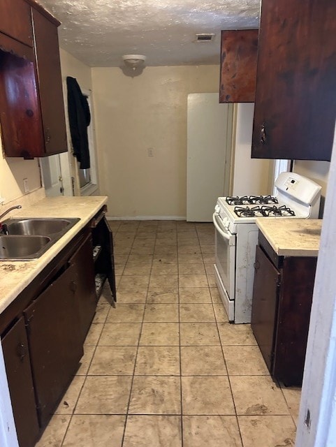 kitchen featuring a textured ceiling, dark brown cabinets, white gas range, and sink