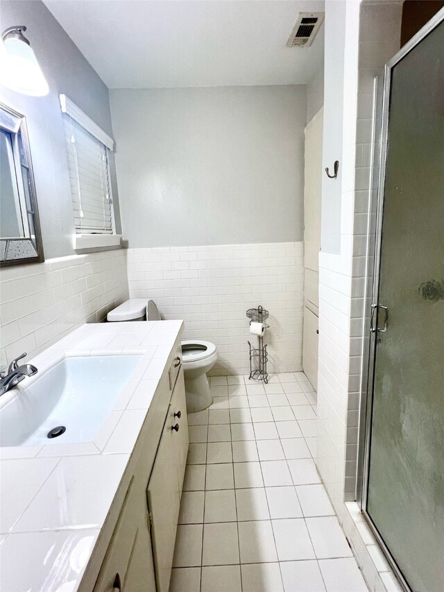 bathroom featuring vanity, a shower with door, tile patterned floors, toilet, and tile walls