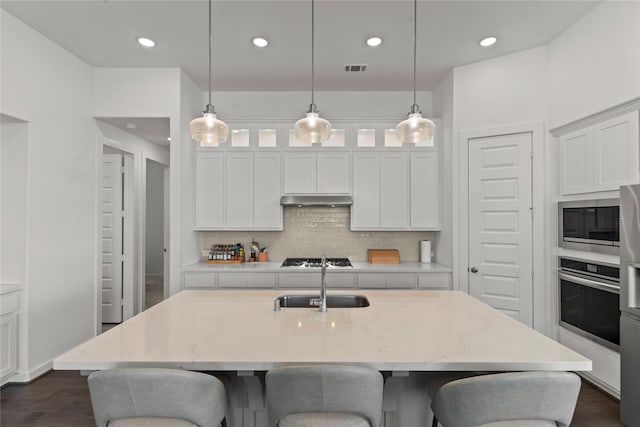 kitchen with appliances with stainless steel finishes, an island with sink, and light stone counters