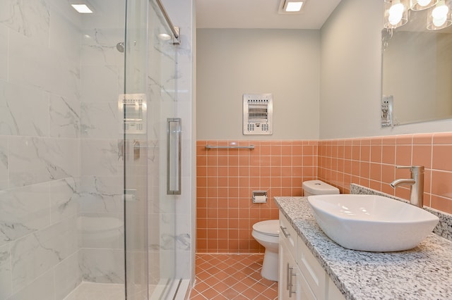 bathroom featuring tile patterned flooring, toilet, vanity, a shower with shower door, and tile walls