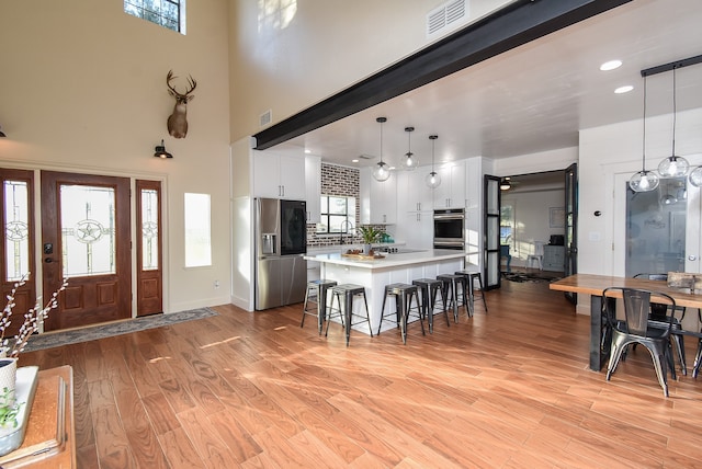 kitchen featuring stainless steel fridge, pendant lighting, white cabinets, light hardwood / wood-style floors, and plenty of natural light