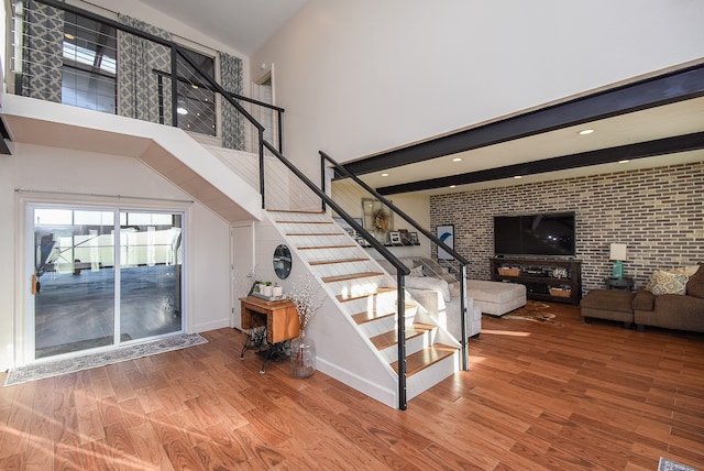 stairs featuring hardwood / wood-style floors, beamed ceiling, brick wall, and a high ceiling