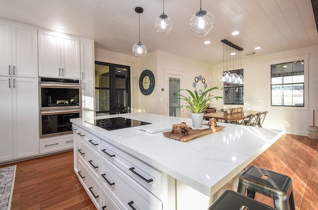 kitchen featuring dark hardwood / wood-style flooring, stainless steel double oven, a kitchen island, and pendant lighting