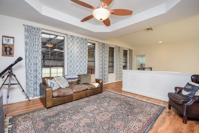 living room featuring wood-type flooring, a tray ceiling, and ceiling fan