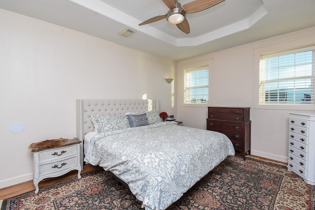 bedroom with a tray ceiling, ceiling fan, and dark wood-type flooring