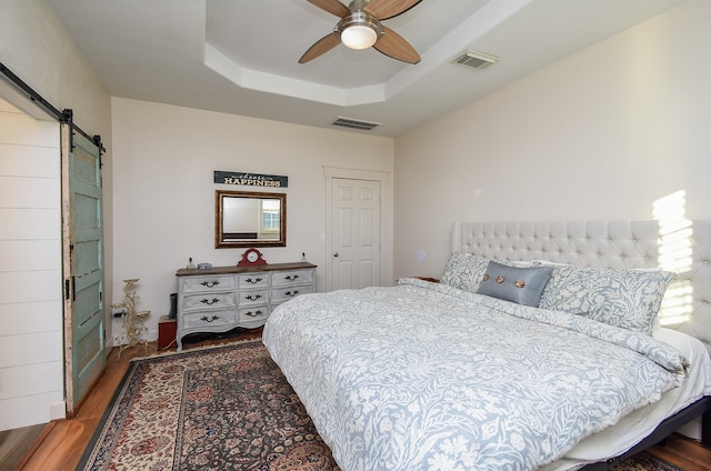 bedroom featuring a raised ceiling, a barn door, ceiling fan, and wood-type flooring