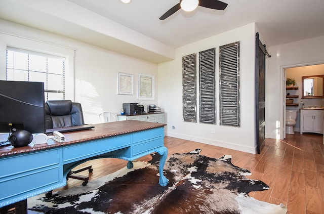 home office featuring hardwood / wood-style floors, a barn door, and ceiling fan