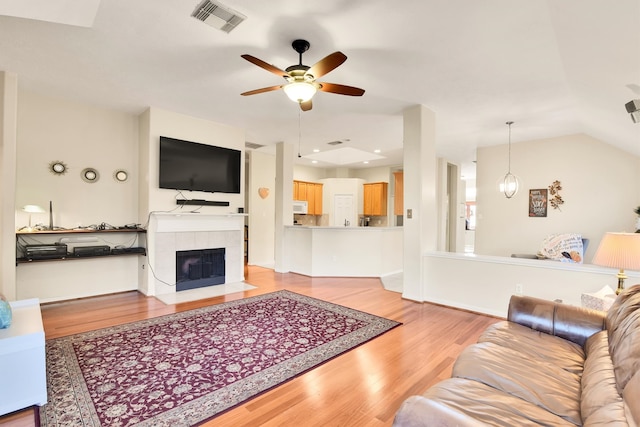 living room featuring ceiling fan, vaulted ceiling, a fireplace, and light hardwood / wood-style flooring