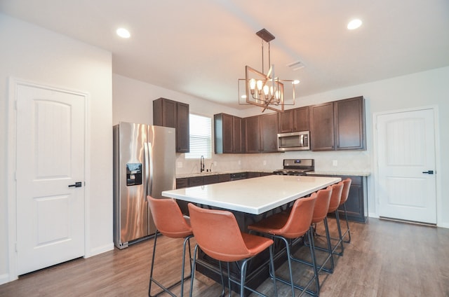 kitchen with appliances with stainless steel finishes, a center island, hardwood / wood-style flooring, and hanging light fixtures