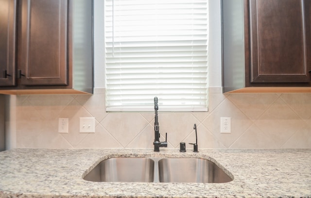 kitchen with tasteful backsplash, dark brown cabinetry, light stone counters, and sink