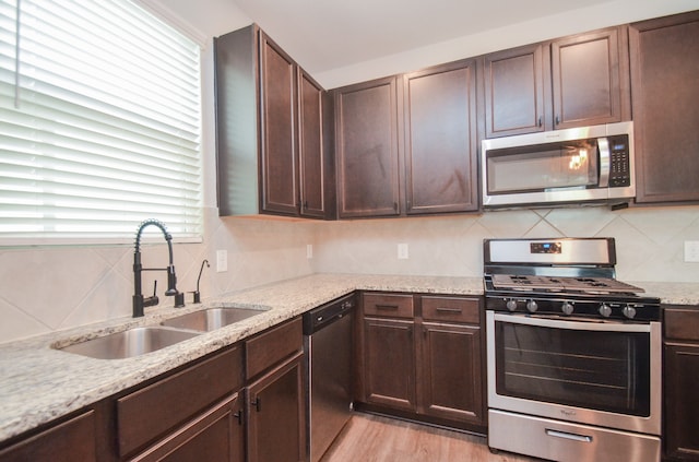 kitchen with light stone countertops, dark brown cabinetry, stainless steel appliances, sink, and light hardwood / wood-style flooring