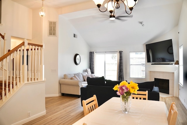 dining room featuring lofted ceiling, light wood-type flooring, a fireplace, and a chandelier