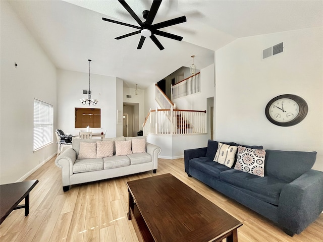 living room with ceiling fan with notable chandelier, high vaulted ceiling, and light hardwood / wood-style flooring