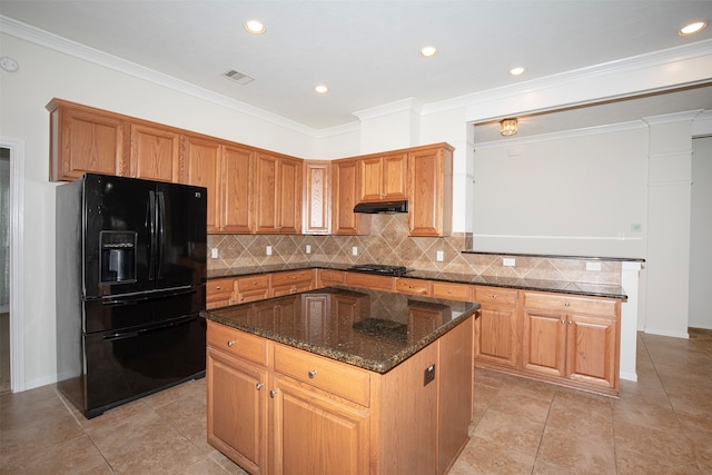 kitchen with a center island, stainless steel gas cooktop, black fridge, dark stone countertops, and crown molding