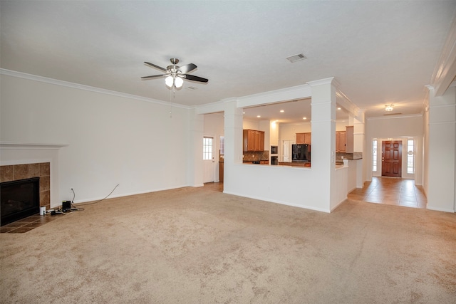 unfurnished living room with ceiling fan, decorative columns, crown molding, a tiled fireplace, and light carpet