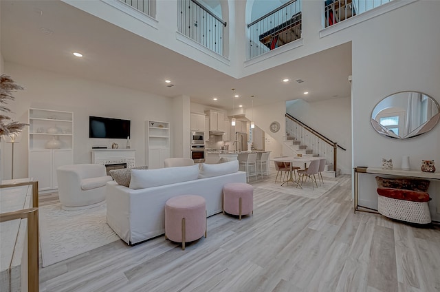 living room featuring built in shelves, a towering ceiling, and light hardwood / wood-style floors