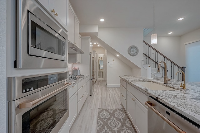 kitchen with pendant lighting, white cabinets, sink, light hardwood / wood-style floors, and stainless steel appliances