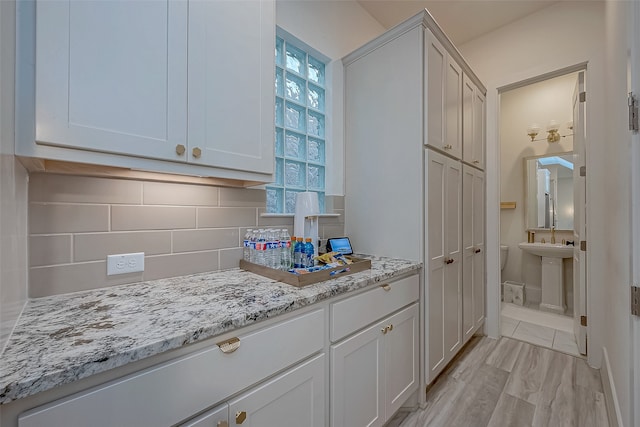 kitchen with tasteful backsplash, white cabinetry, a healthy amount of sunlight, and light stone counters