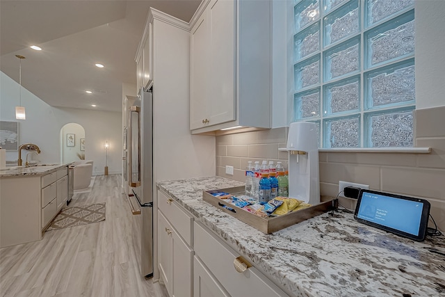 kitchen with backsplash, hanging light fixtures, light stone countertops, light wood-type flooring, and white cabinetry