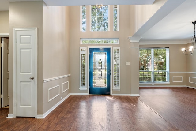 foyer entrance with wood-type flooring, an inviting chandelier, ornamental molding, and ornate columns