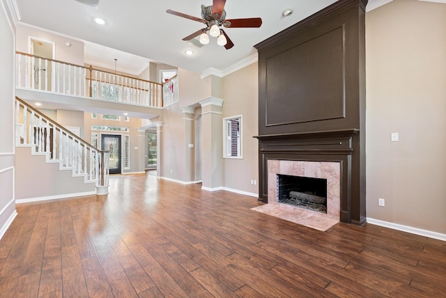 unfurnished living room featuring a high ceiling, decorative columns, hardwood / wood-style floors, a fireplace, and ornamental molding