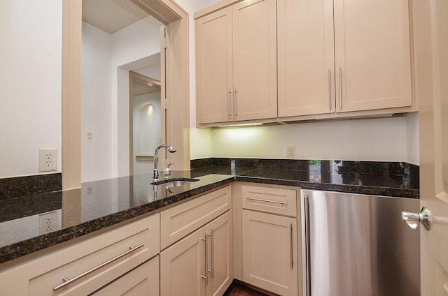 kitchen with stainless steel refrigerator, dark stone countertops, cream cabinets, and sink