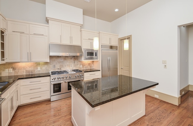 kitchen featuring light wood-type flooring, built in appliances, a kitchen island, and dark stone counters